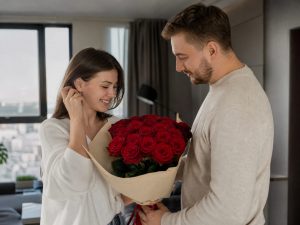 13 роз — мужчина дарит жене пышный букет из 13 роз красных Red Naomi в кремовой упаковке на годовщину в современной квартире
