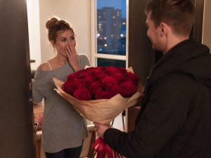 17 роз — мужчина дарит жене пышный букет из 17 роз красных Red Naomi в кремовой упаковке на годовщину в современной квартире