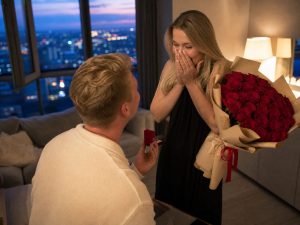 21 роза — мужчина дарит жене пышный букет из 21 розу красных Red Naomi в кремовой упаковке на годовщину в современной квартире