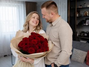 23 розы — мужчина дарит жене пышный букет из 23 розы красных Red Naomi в кремовой упаковке на годовщину в современной квартире