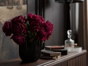 Бордовые пионы — букет в чёрной керамической вазе на тёмном комоде в стиле дарк-академия в люксовом интерьере