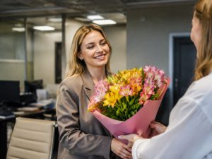 Девушка в офисе получает букет альстромерий от коллеги