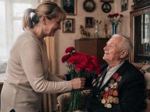 Внучка дарит букет красных гвоздик дедушке-ветерану